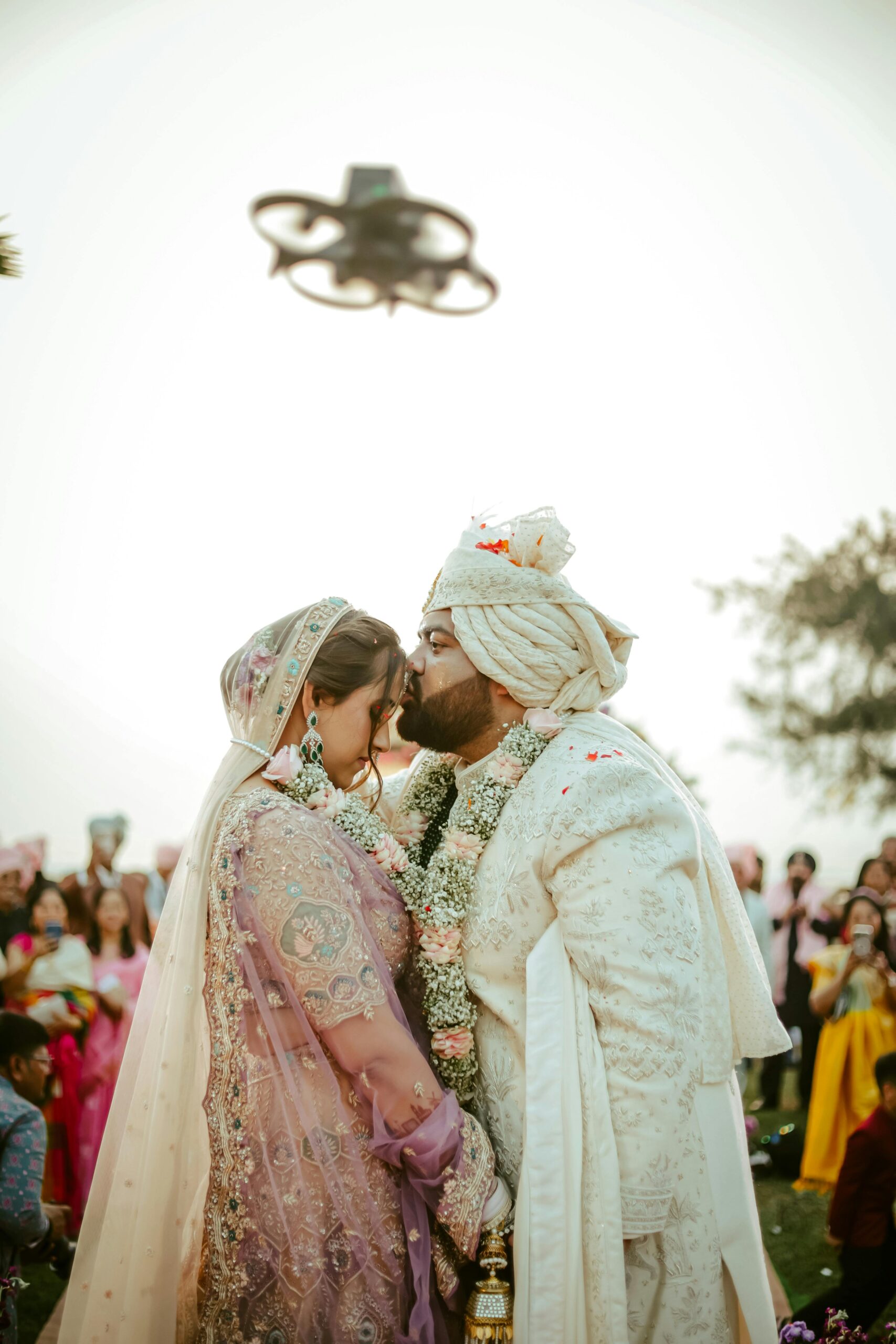 A loving couple embraces during their wedding ceremony in India, surrounded by guests.